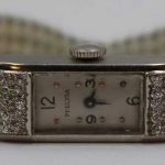Art Deco platinum and tiered diamond Precisa watch face suspended from a multi-row seed pearl bracelet
